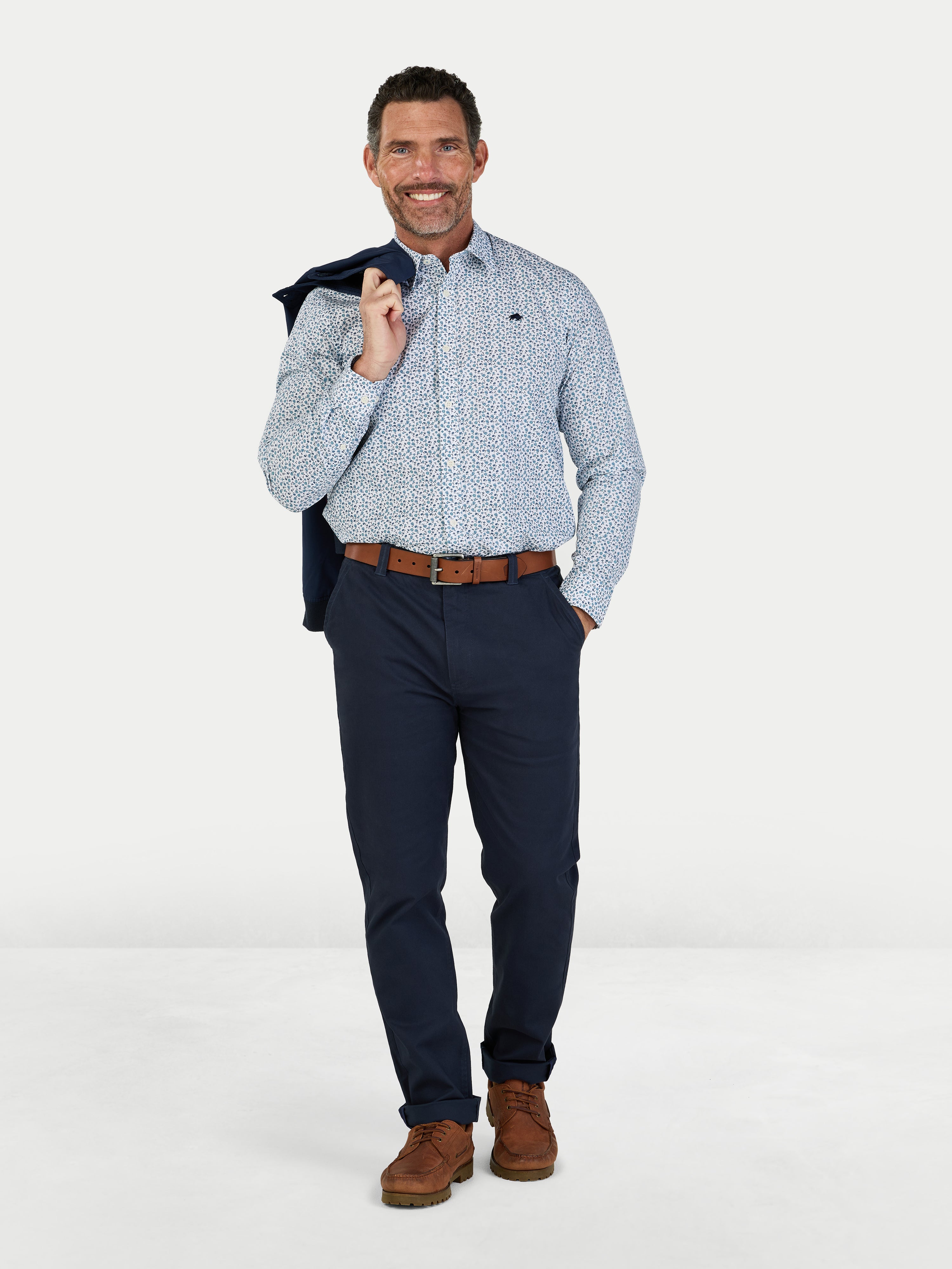 Man wearing a patterned shirt, navy pants, and brown shoes on a white background