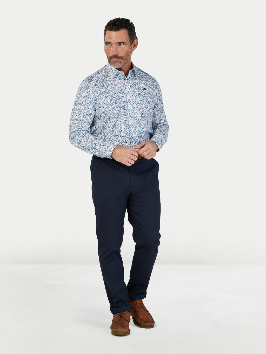 Man wearing a patterned shirt and navy pants on a white background