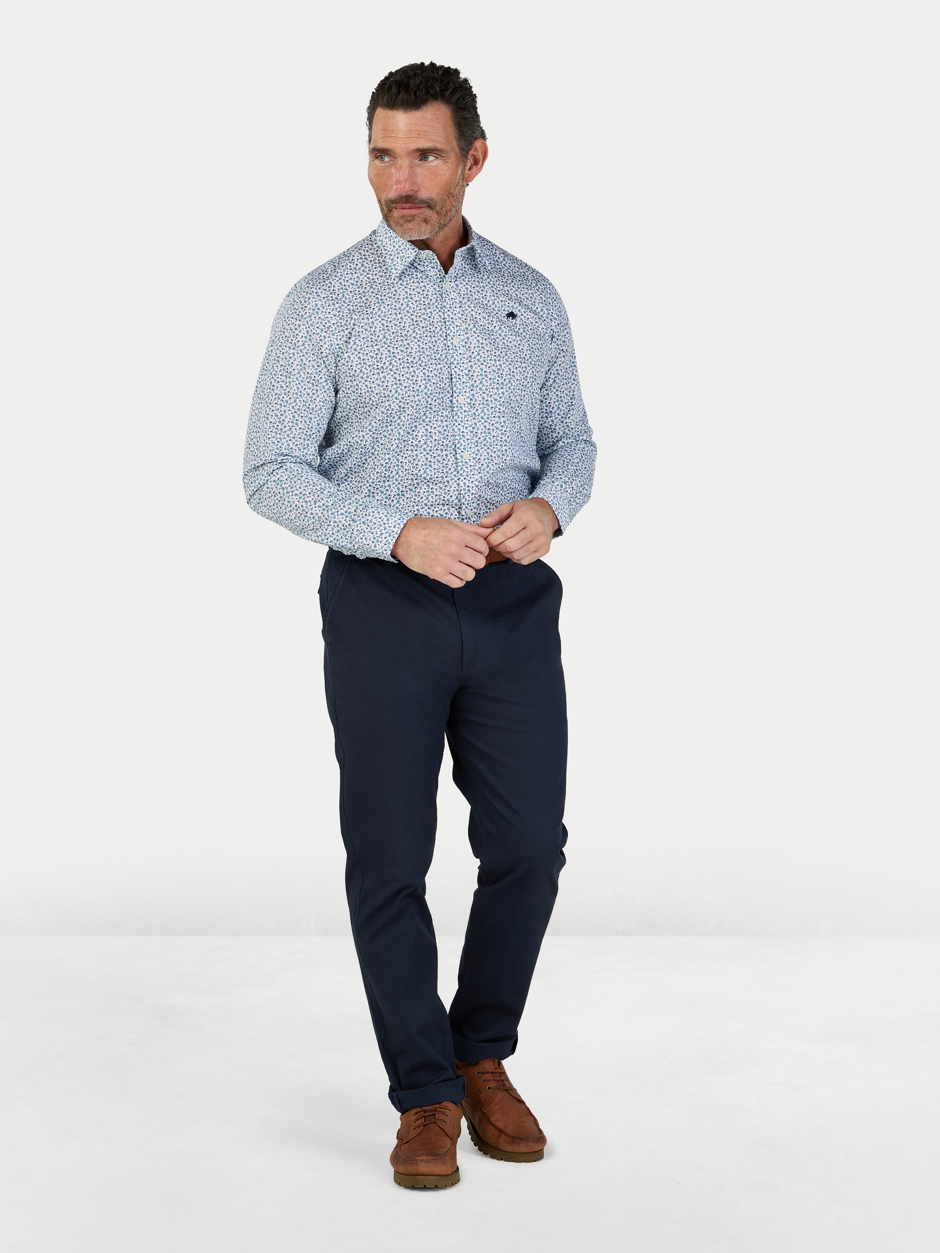 Man wearing a patterned shirt and navy pants on a white background