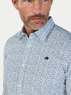 Man wearing a patterned shirt with a visible brand logo on a light background