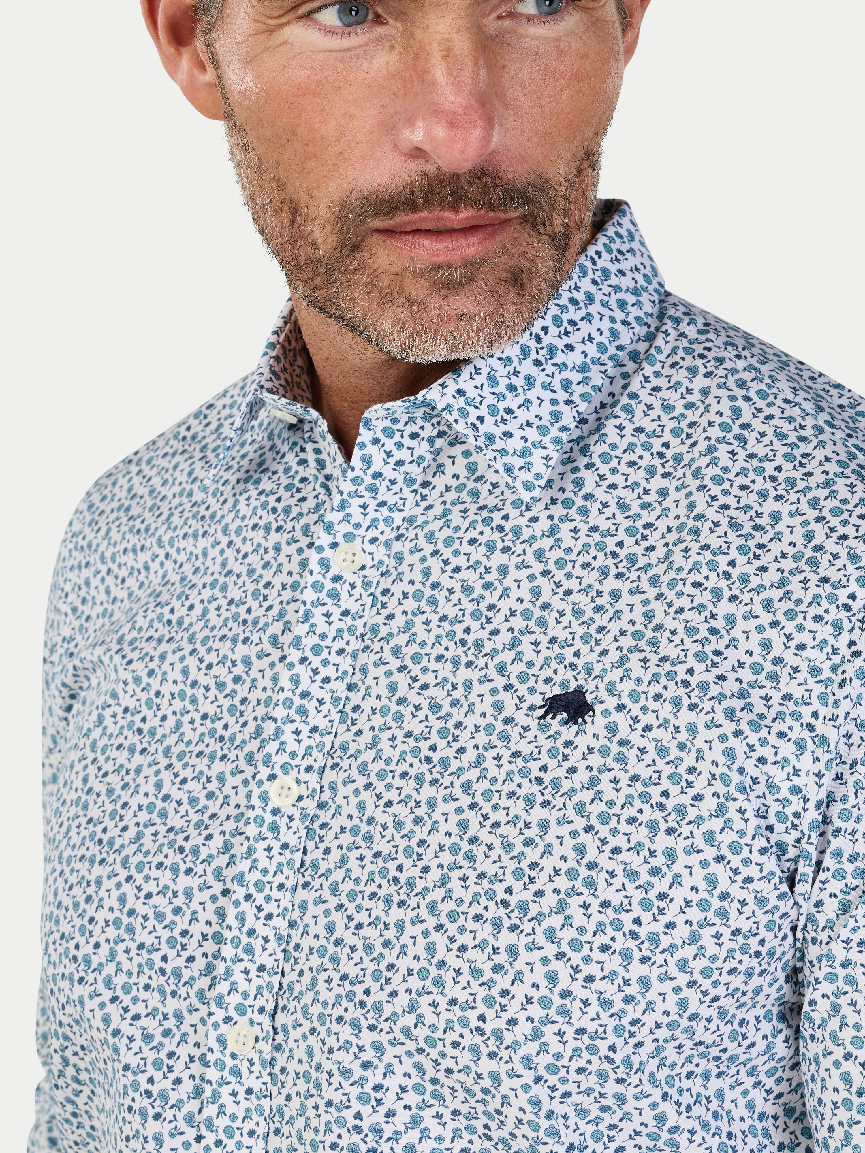 Man wearing a patterned shirt with a visible brand logo on a light background
