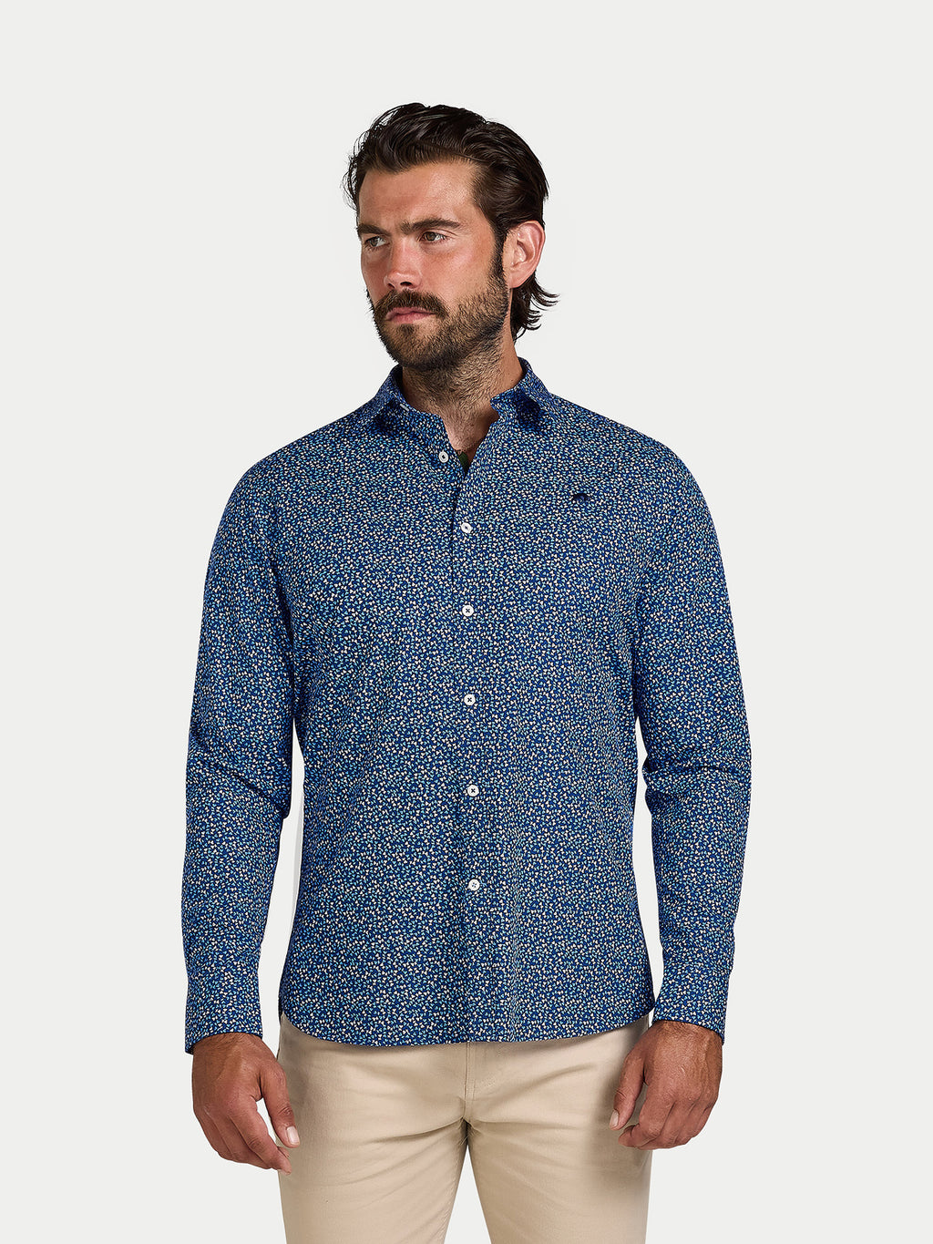 Man wearing a blue patterned shirt and beige pants on a white background