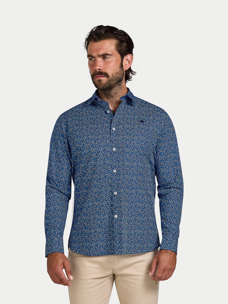 Man wearing a blue patterned shirt and beige pants on a white background