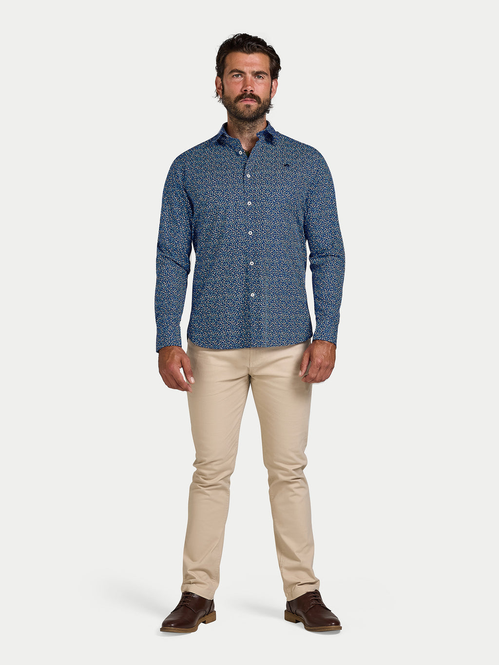 Man wearing a blue patterned shirt and beige pants on a white background