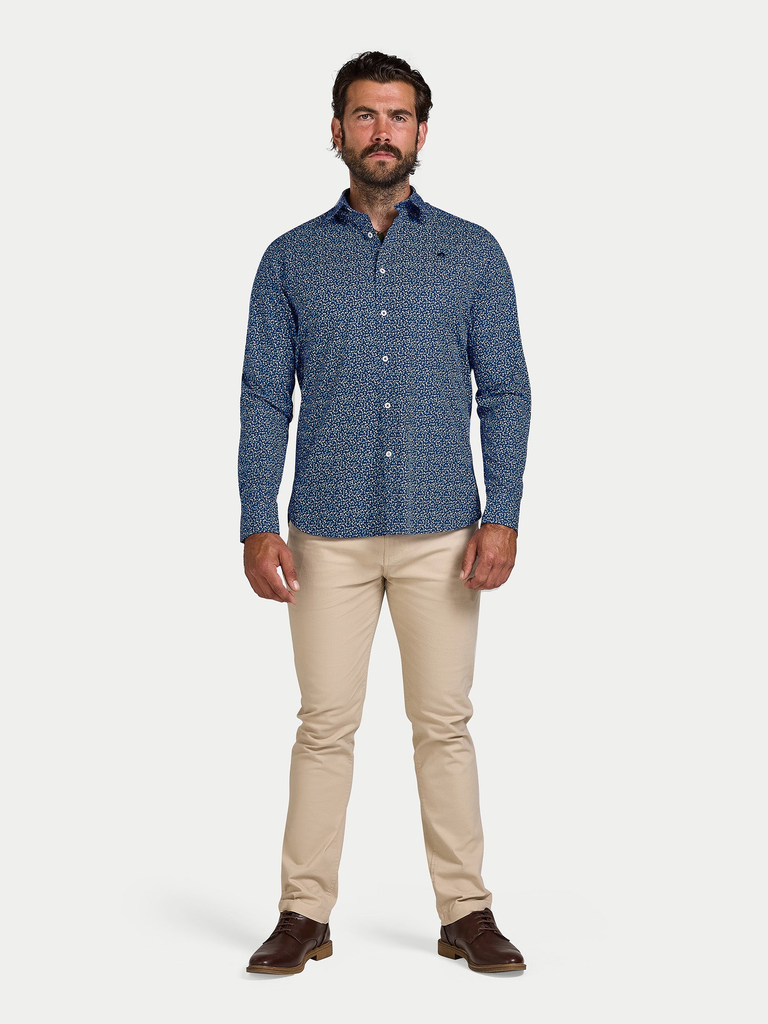 Man wearing a blue patterned shirt and beige pants on a white background