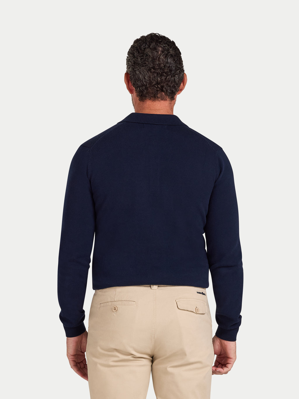 Man wearing a navy sweater and beige pants on a light gray background
