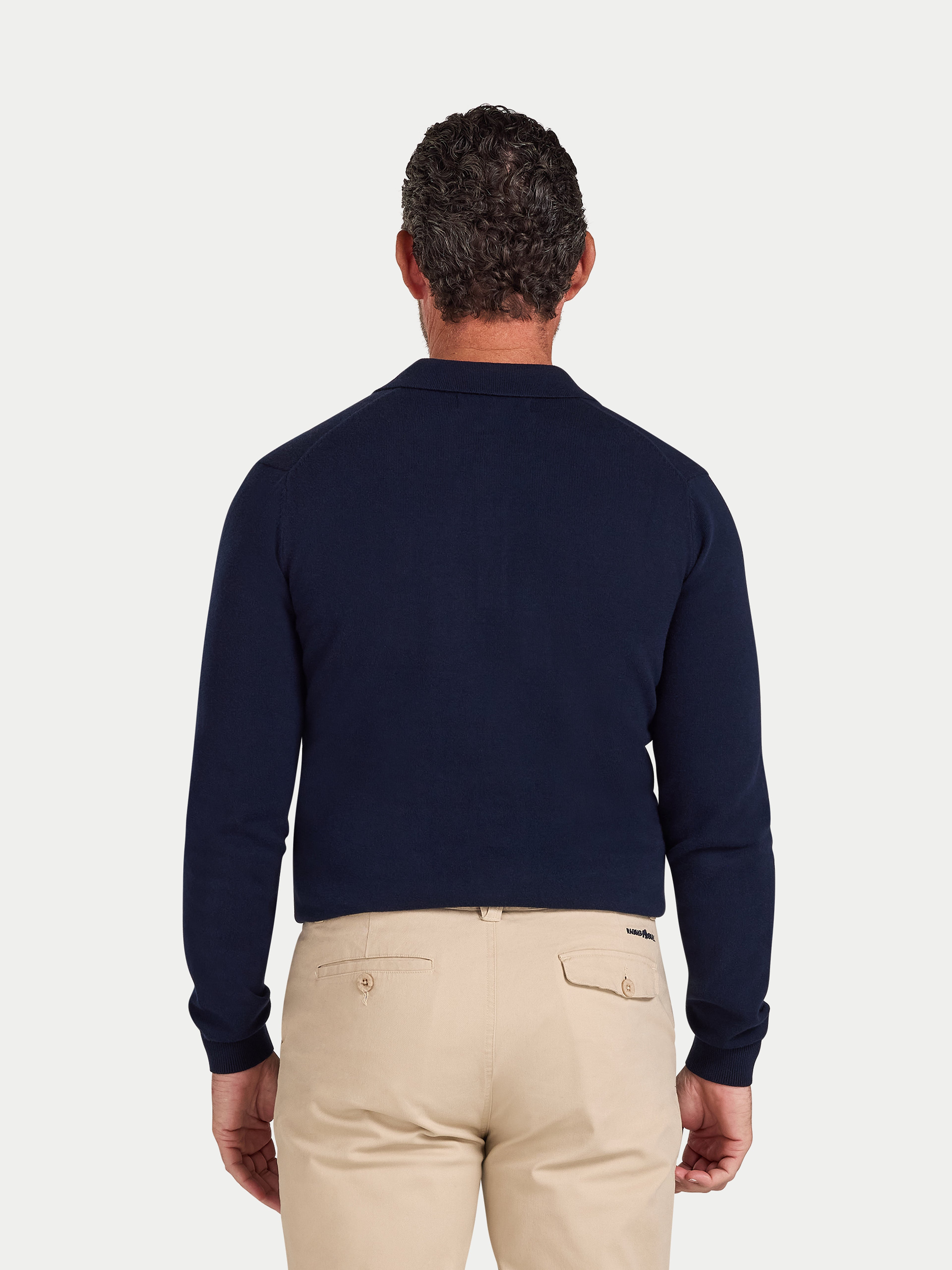 Man wearing a navy sweater and beige pants on a light gray background