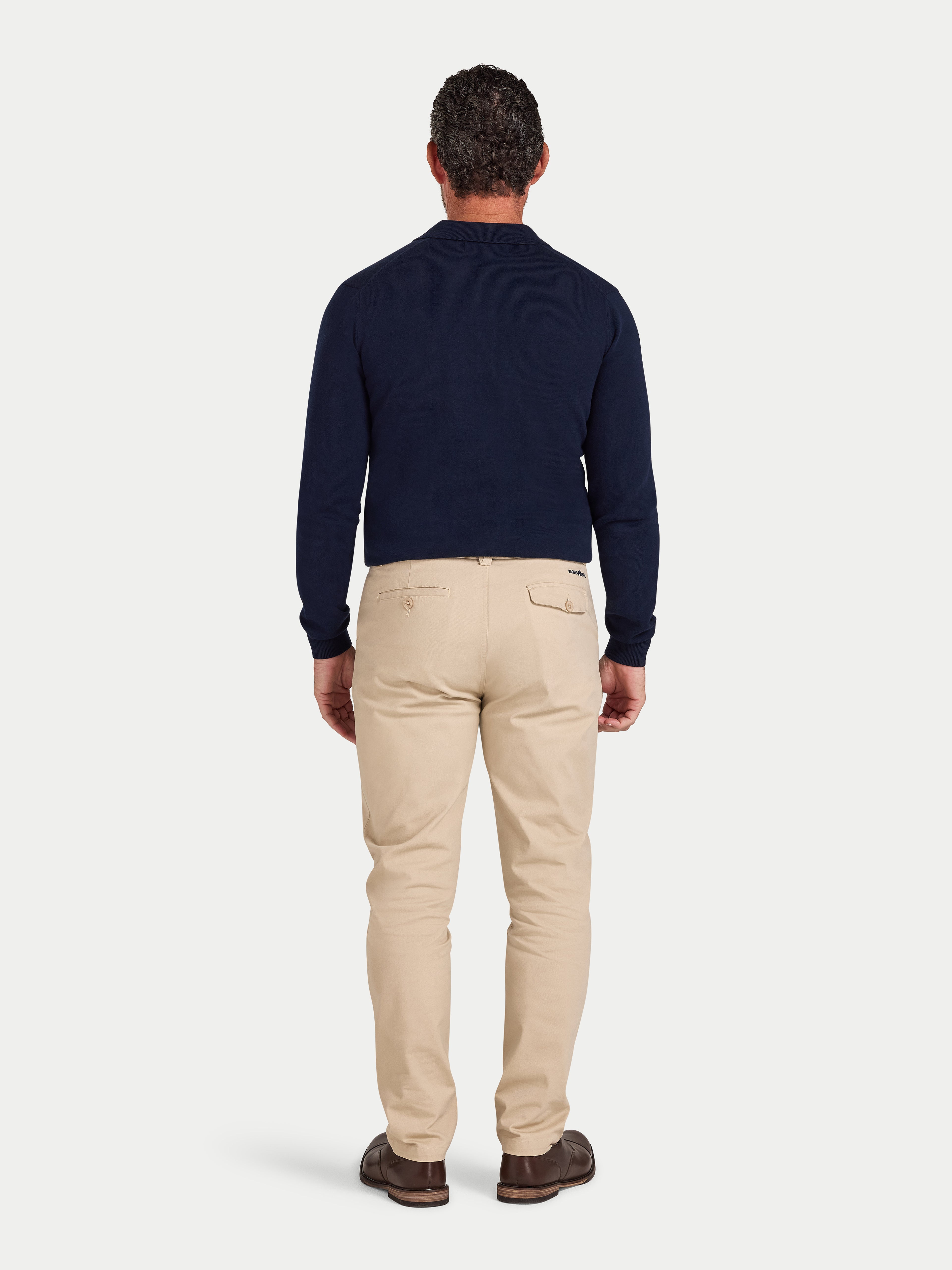 Man wearing a navy sweater and beige pants on a light gray background