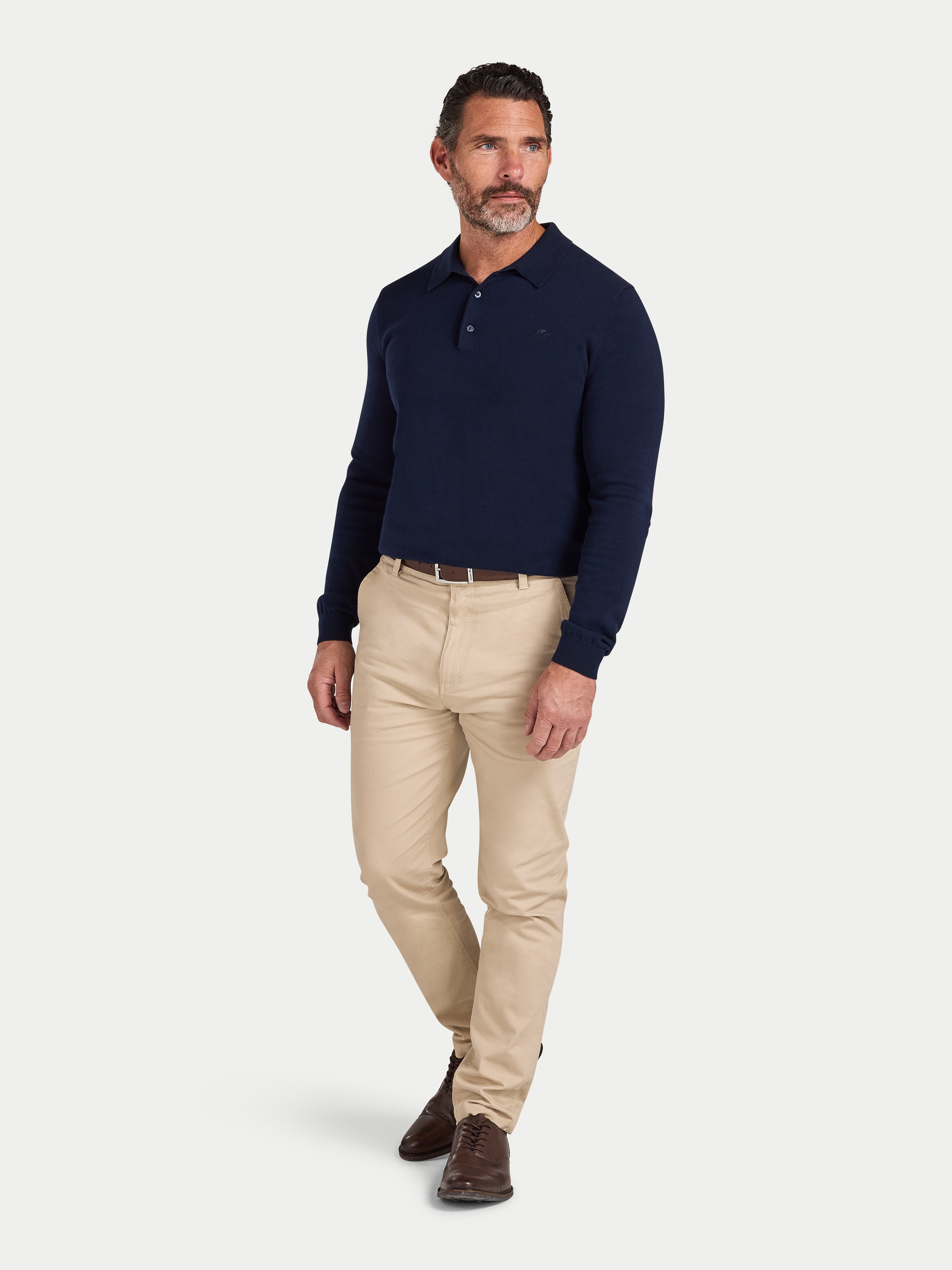 Man wearing a navy long-sleeve polo shirt and beige pants on a light gray background