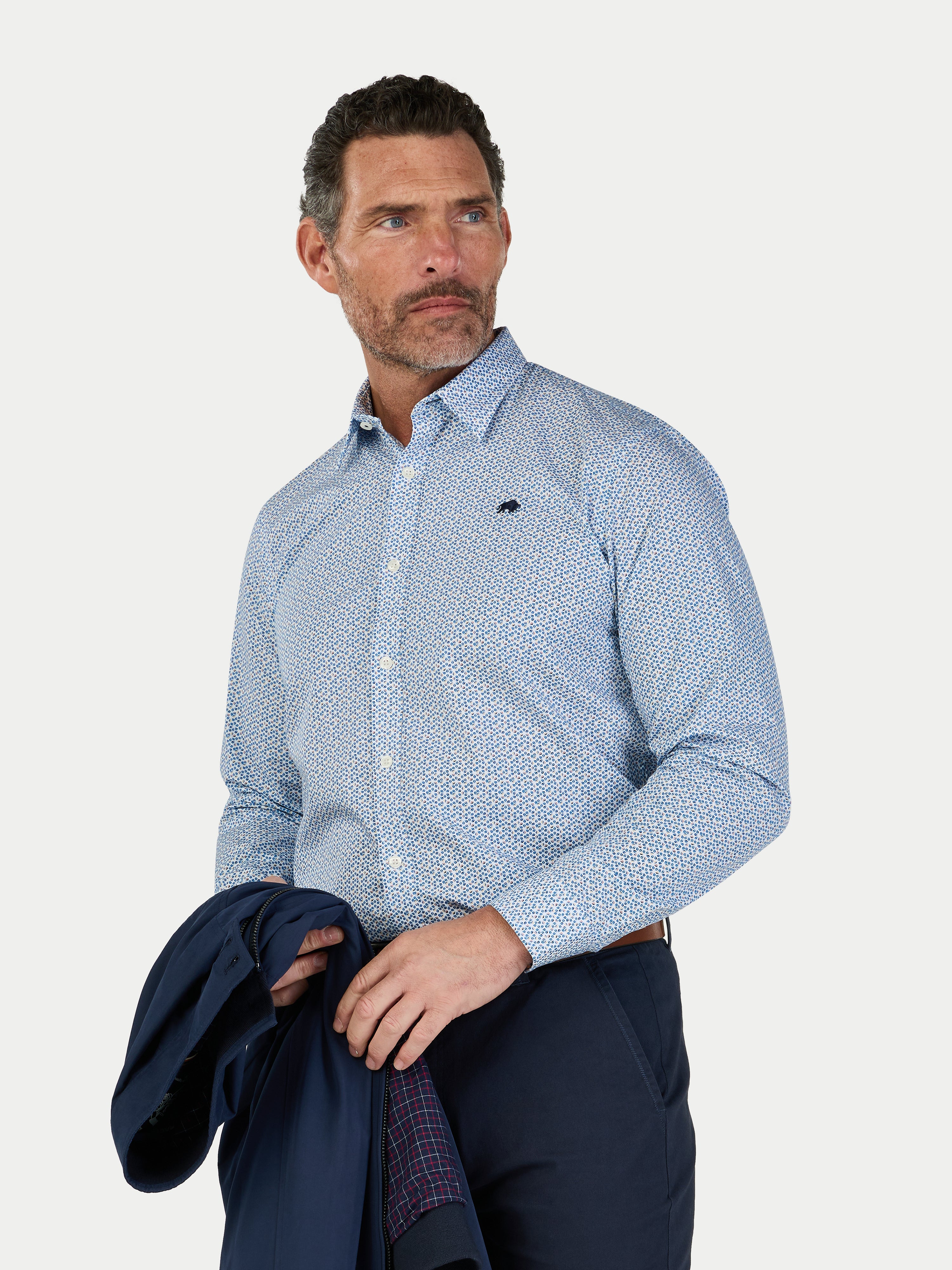 Man wearing a blue patterned shirt holding a jacket on a white background