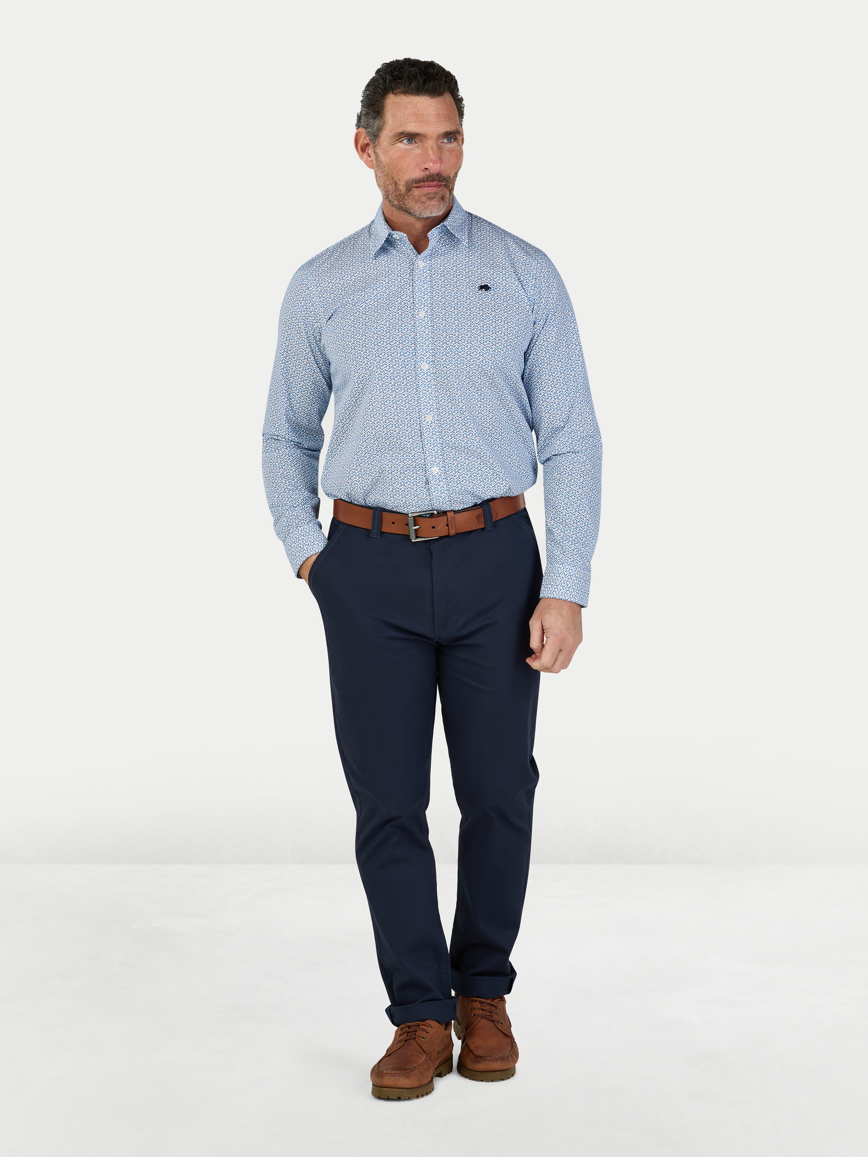 Man wearing a light blue checkered shirt, navy pants, and brown shoes on a white background