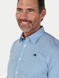 Man wearing a blue patterned shirt with a visible Raging Bull logo on a white background