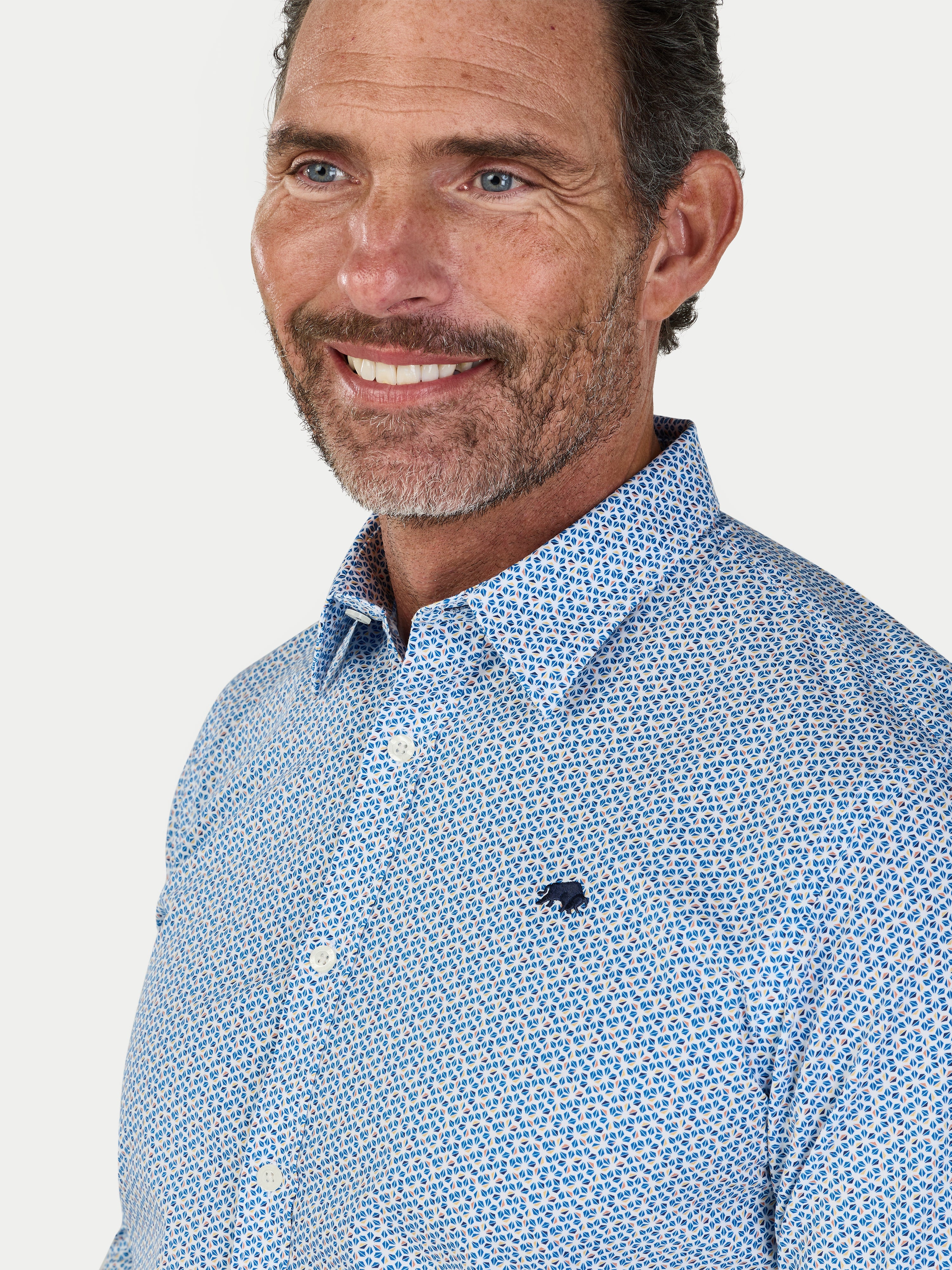 Man wearing a blue patterned shirt with a visible Raging Bull logo on a white background