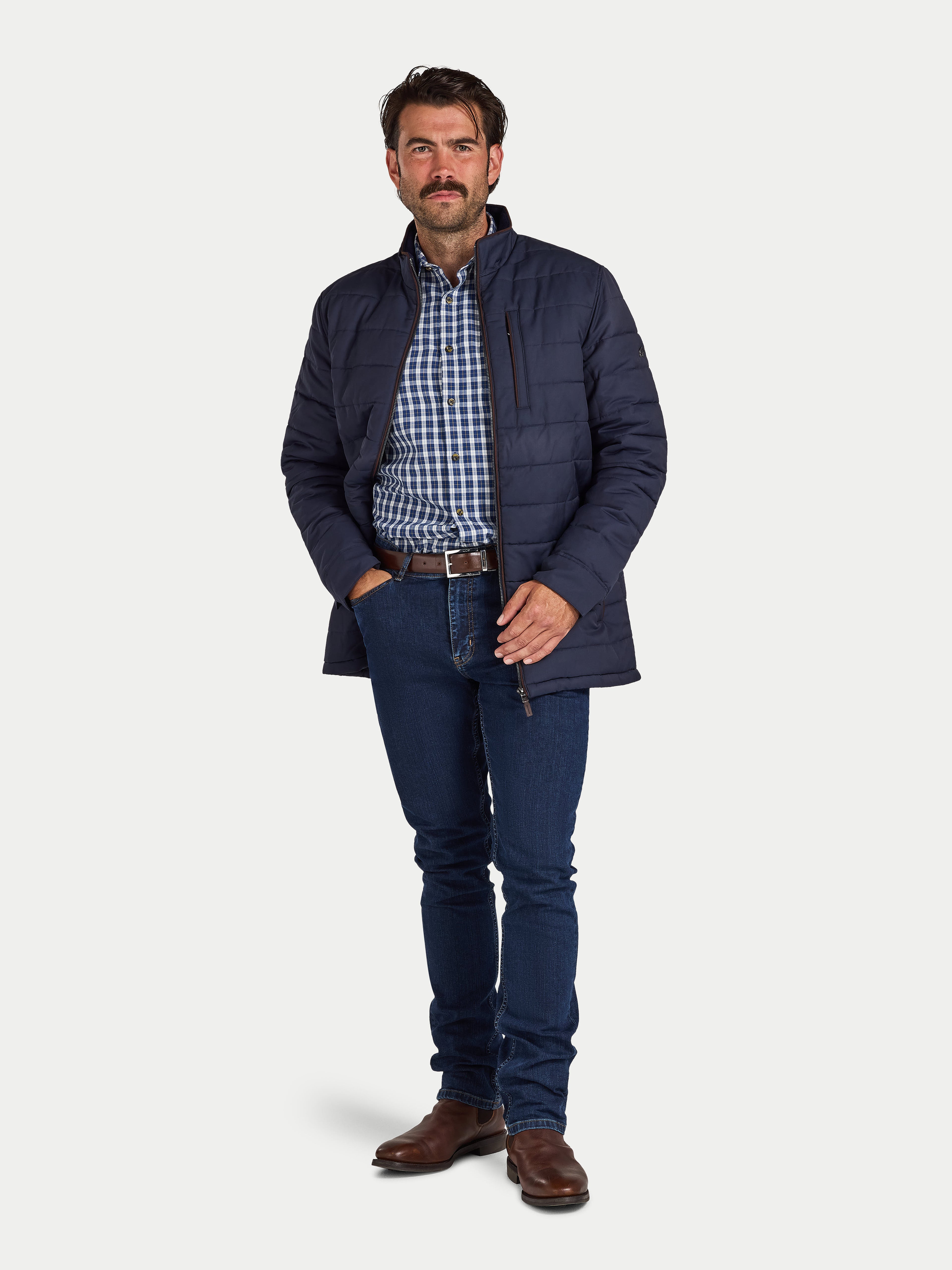 Man wearing a navy puffer jacket, checkered shirt, and jeans on a white background