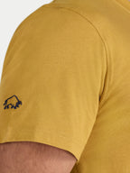 Close-up of a mustard yellow t-shirt with a small logo on the sleeve.