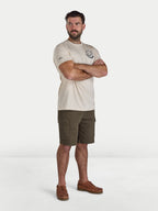 Man wearing a beige t-shirt and green shorts standing against a white background