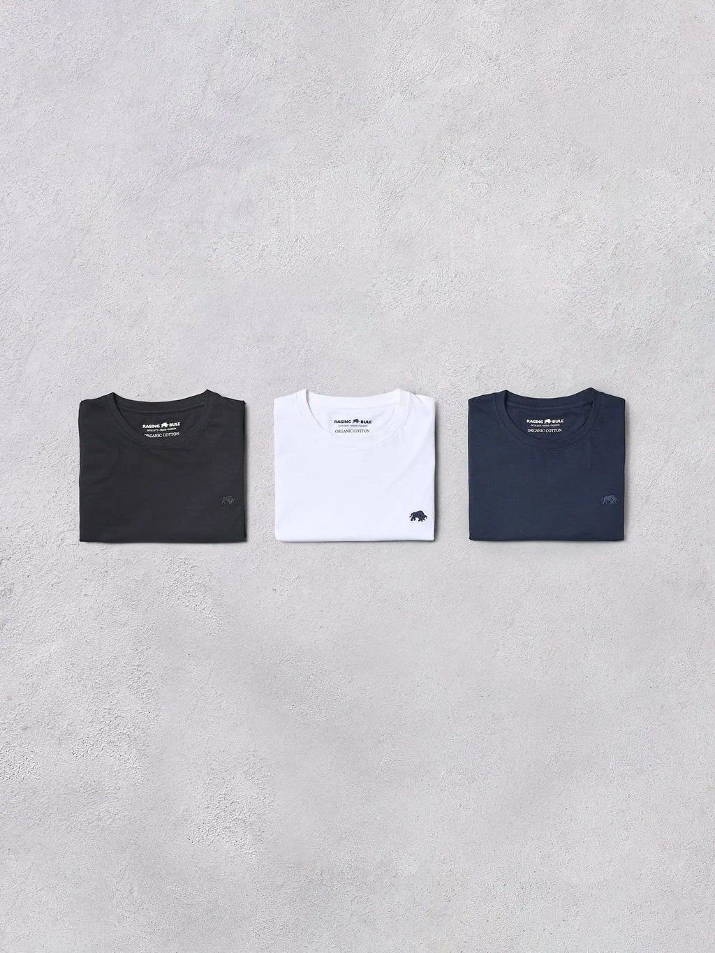 Three Raging Bull t-shirts in black, white, and navy on a gray background