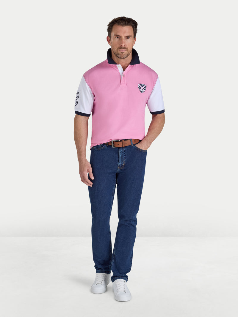 Man wearing a pink and white polo shirt with blue jeans on a white background