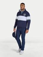 Man wearing a navy and white striped sweater with a logo, holding a blue cap on a white background