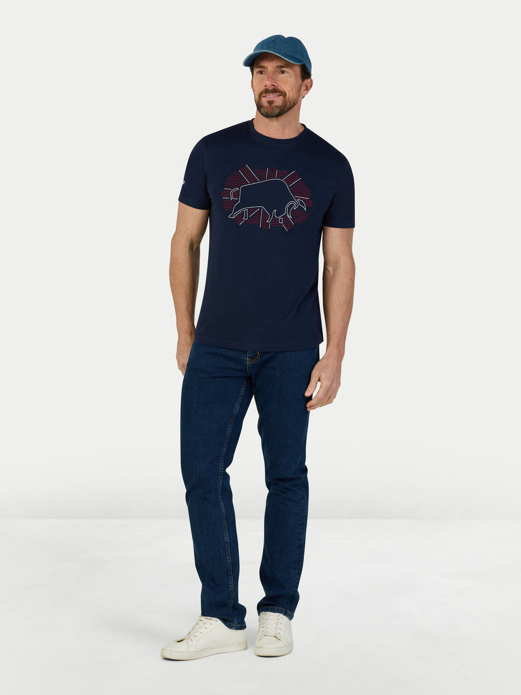 Man wearing a navy t-shirt with a graphic design, blue jeans, and a cap on a white background