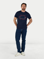 Man wearing a navy t-shirt with a graphic design and dark jeans on a white background