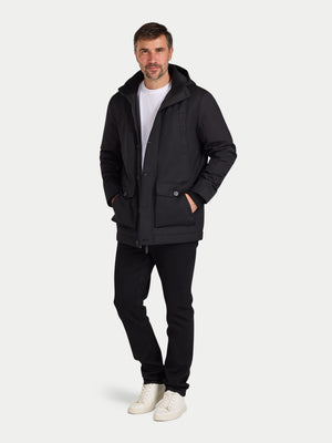 Man wearing a black coat, white shirt, black pants, and white shoes on a light gray background