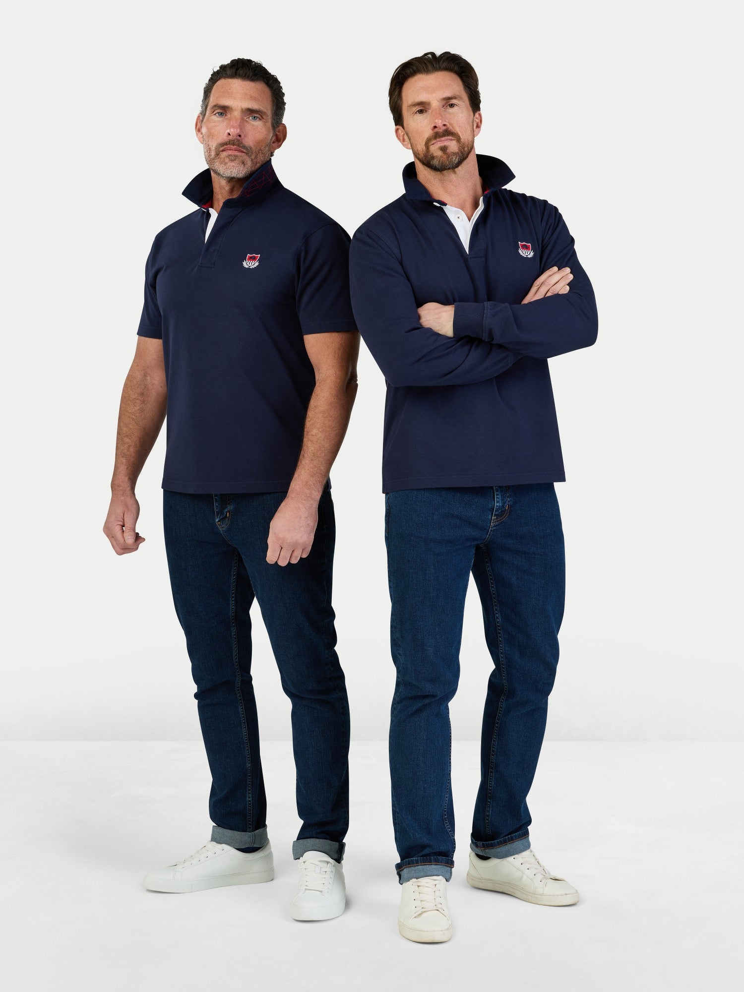 Two men wearing navy jackets and jeans standing against a white background