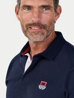 Man wearing a navy polo shirt with a logo on a light gray background