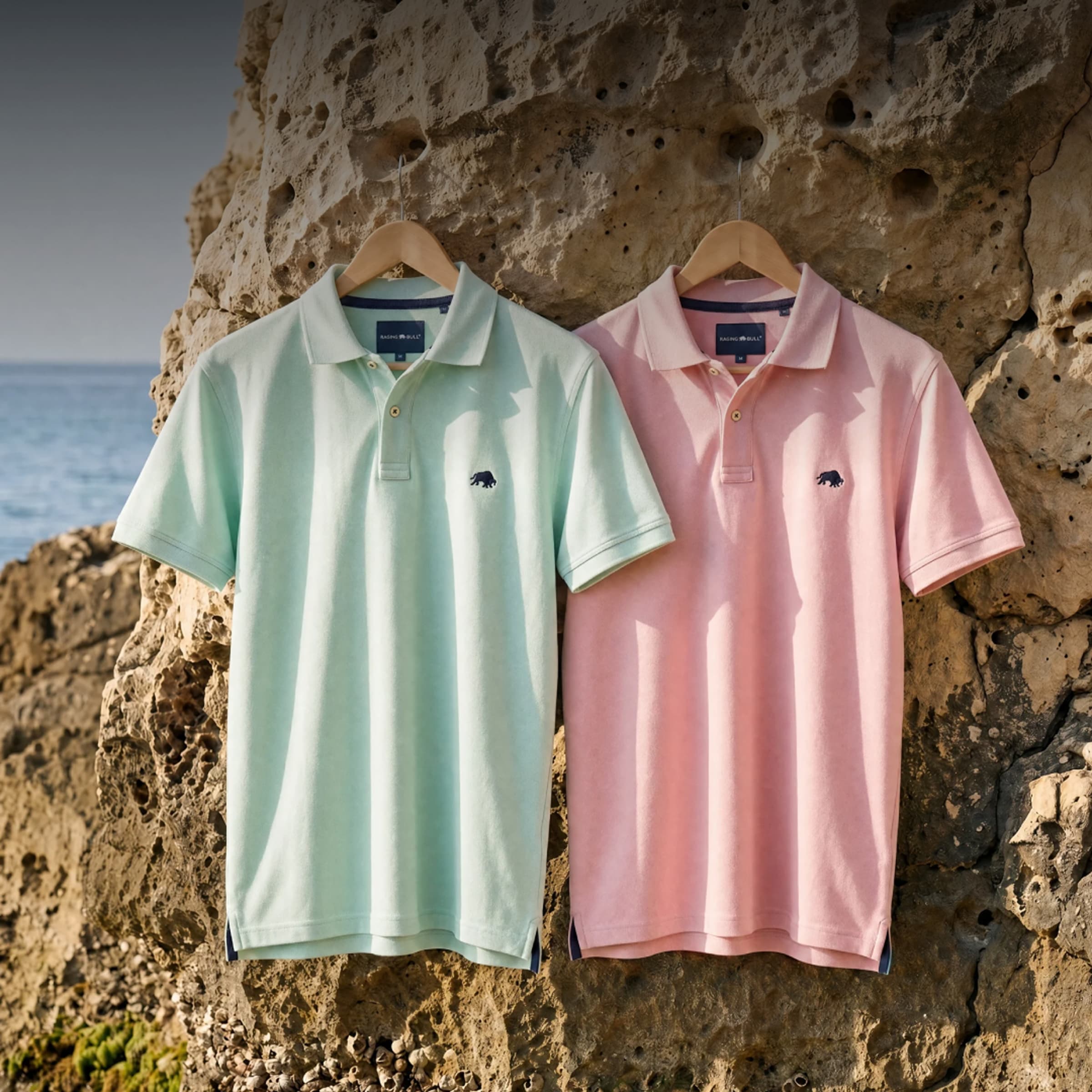 Raging Bull Classic Organic Polo in apple green and pink tops on a rock wall with the sea in the background.