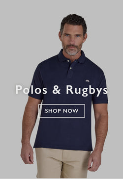 Man in a striped polo shirt and cap adjusting his hat outdoors by a river.