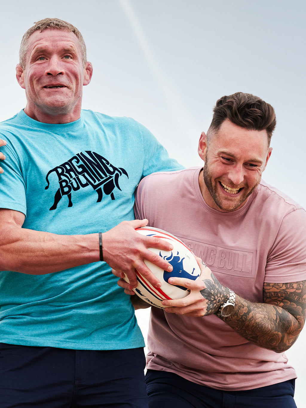 Two men playing around and holding a Raging Bull rugby ball. 