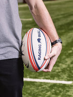 A person holding a Raging Bull rugby ball on pitch. 