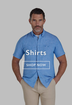 Man in a light check shirt and jeans standing by a car near a river, holding a duffel bag.