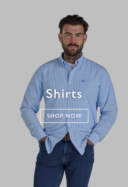 Man in a light check shirt and jeans standing by a car near a river, holding a duffel bag.