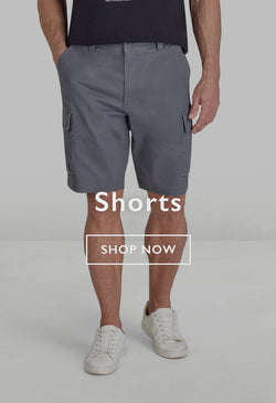 Two men wearing casual shorts and sneakers standing outdoors on a forest path.