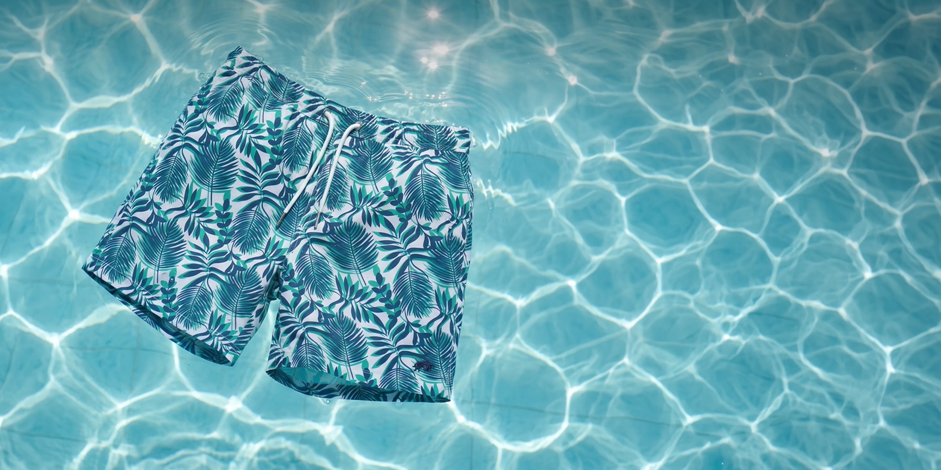 Raging Bull Hawaiian Patterned Swim Short in green in a shimmering pool. 