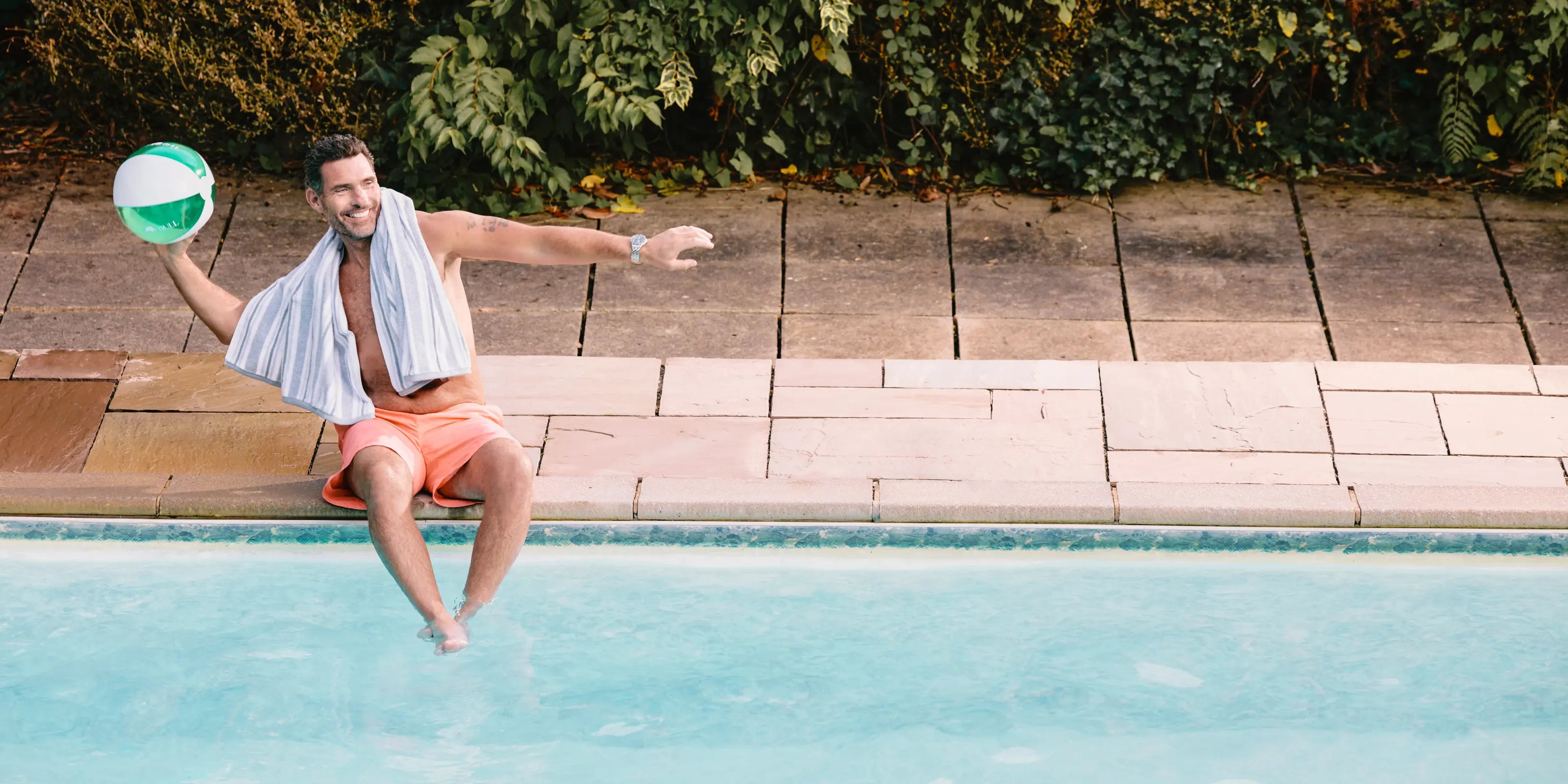 Man playing with a beach ball by a pool wearing Raging Bull Swimshorts in Coral.