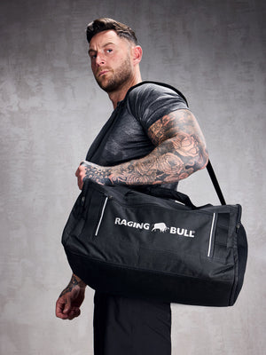 A man carrying a black Raging Bull duffel bag. 