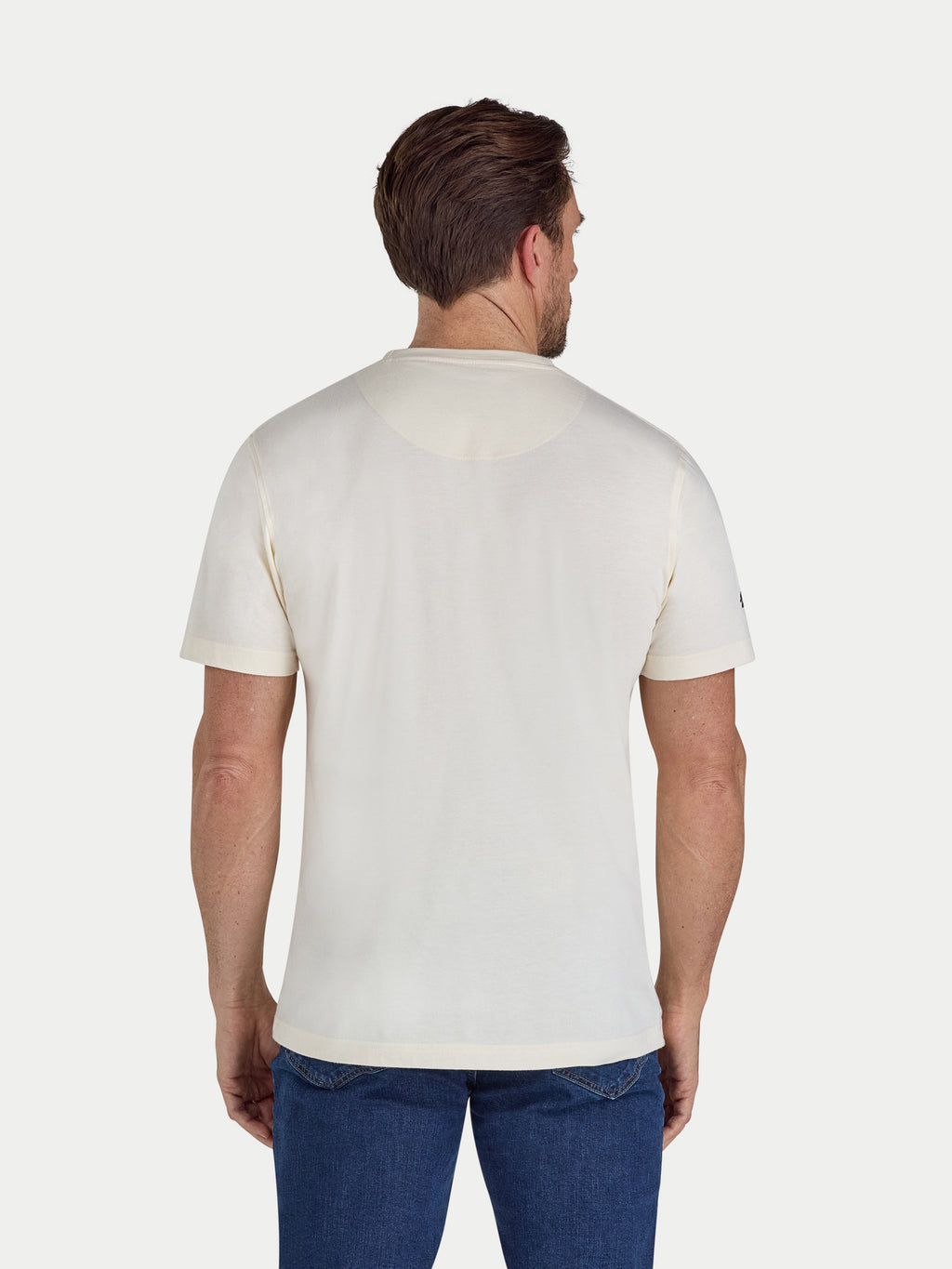 Man wearing a plain white t-shirt and blue jeans on a light gray background