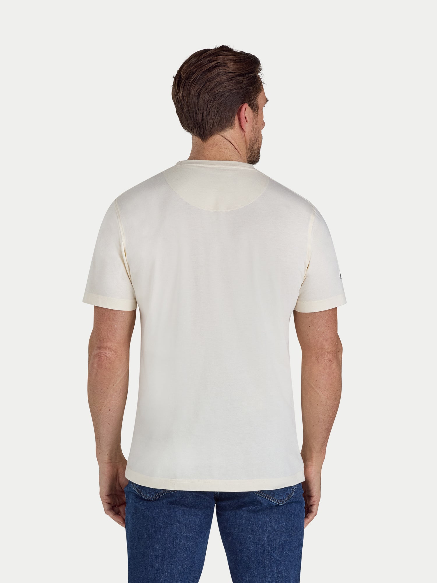 Man wearing a plain white t-shirt and blue jeans on a light gray background