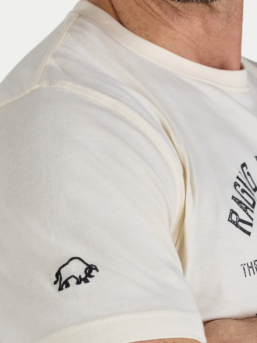 Close-up of a person wearing a white t-shirt with a logo and text on a plain background