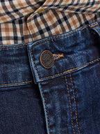 Close-up of a button on blue jeans with a plaid shirt in the background
