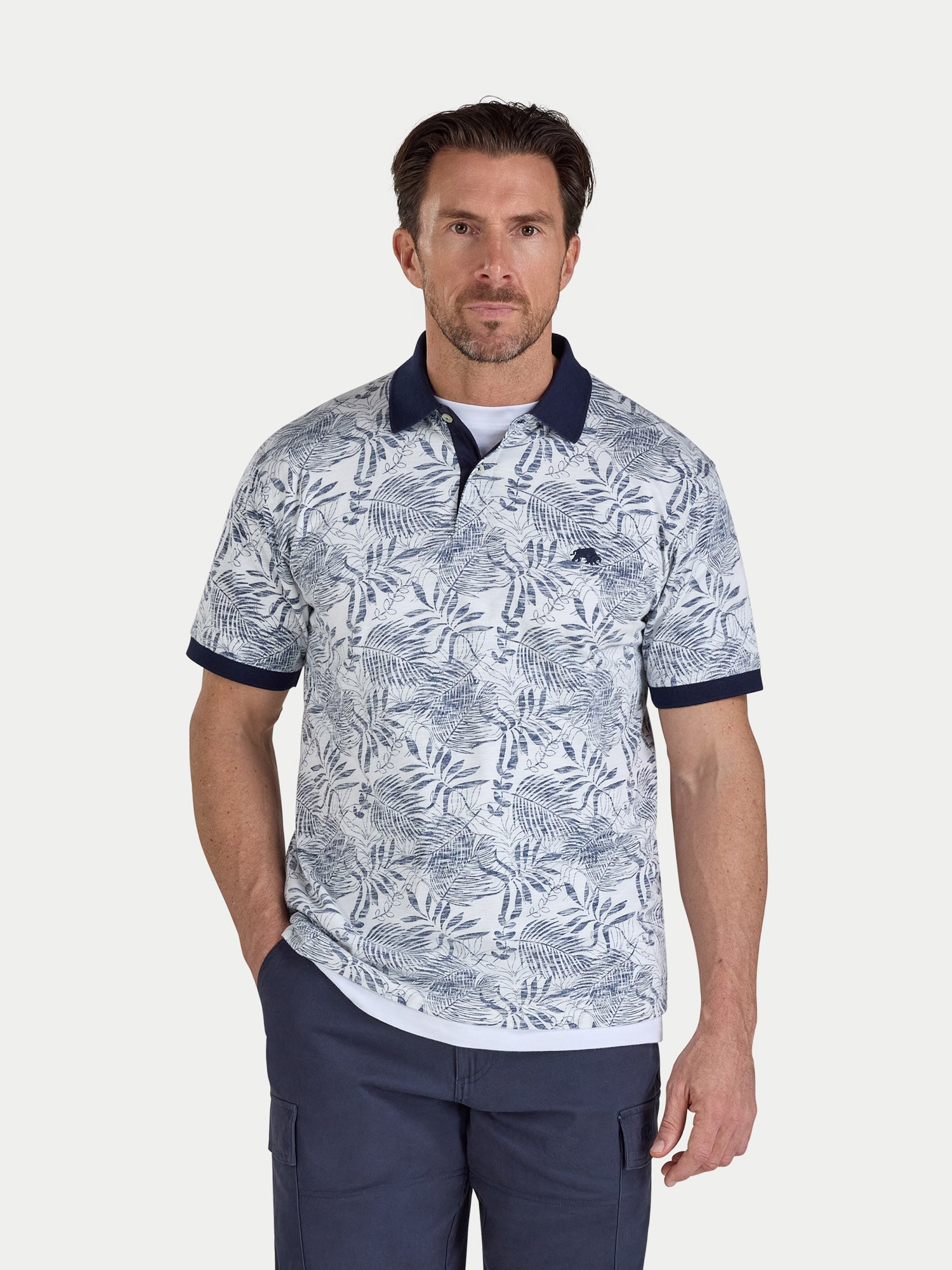 Man wearing a patterned polo shirt and navy pants on a white background