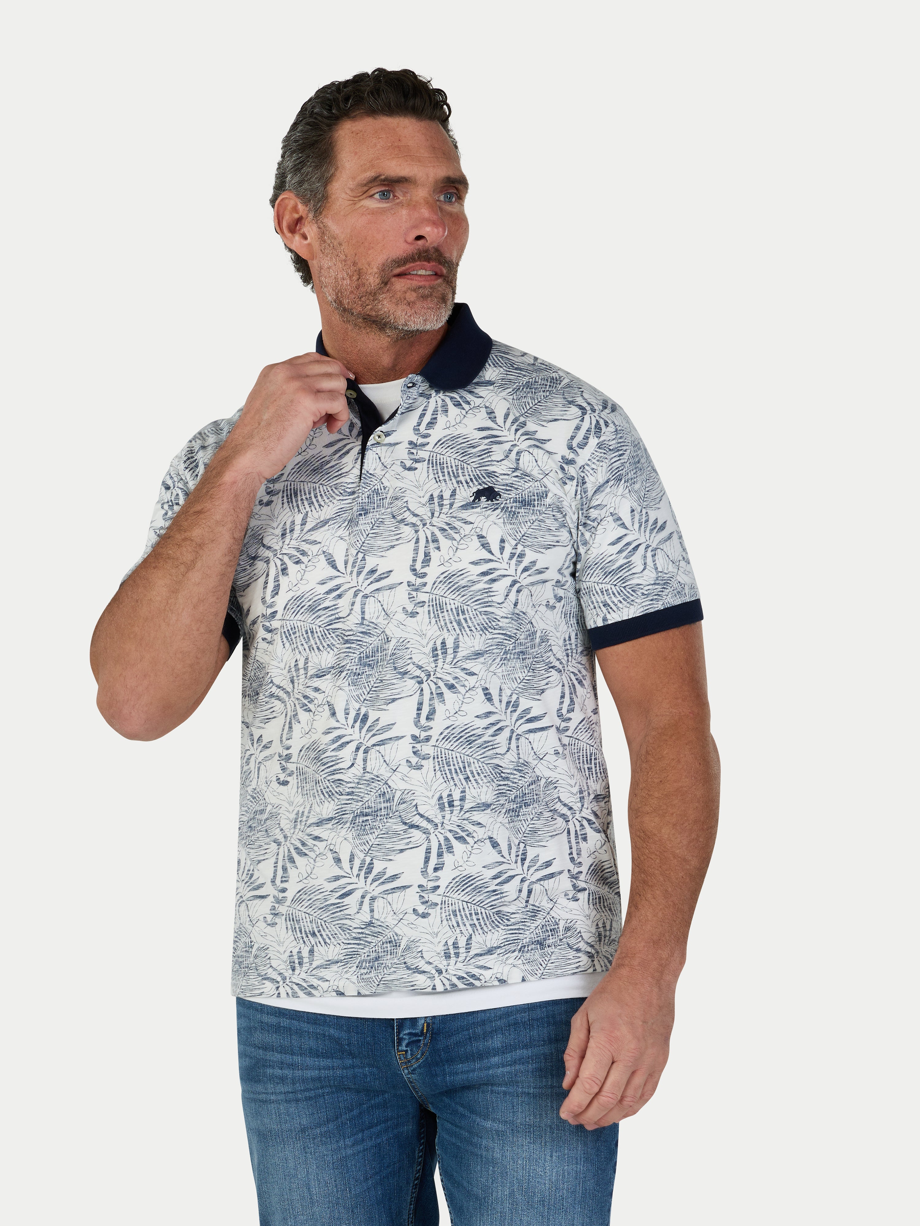 Man wearing a patterned polo shirt and jeans on a white background