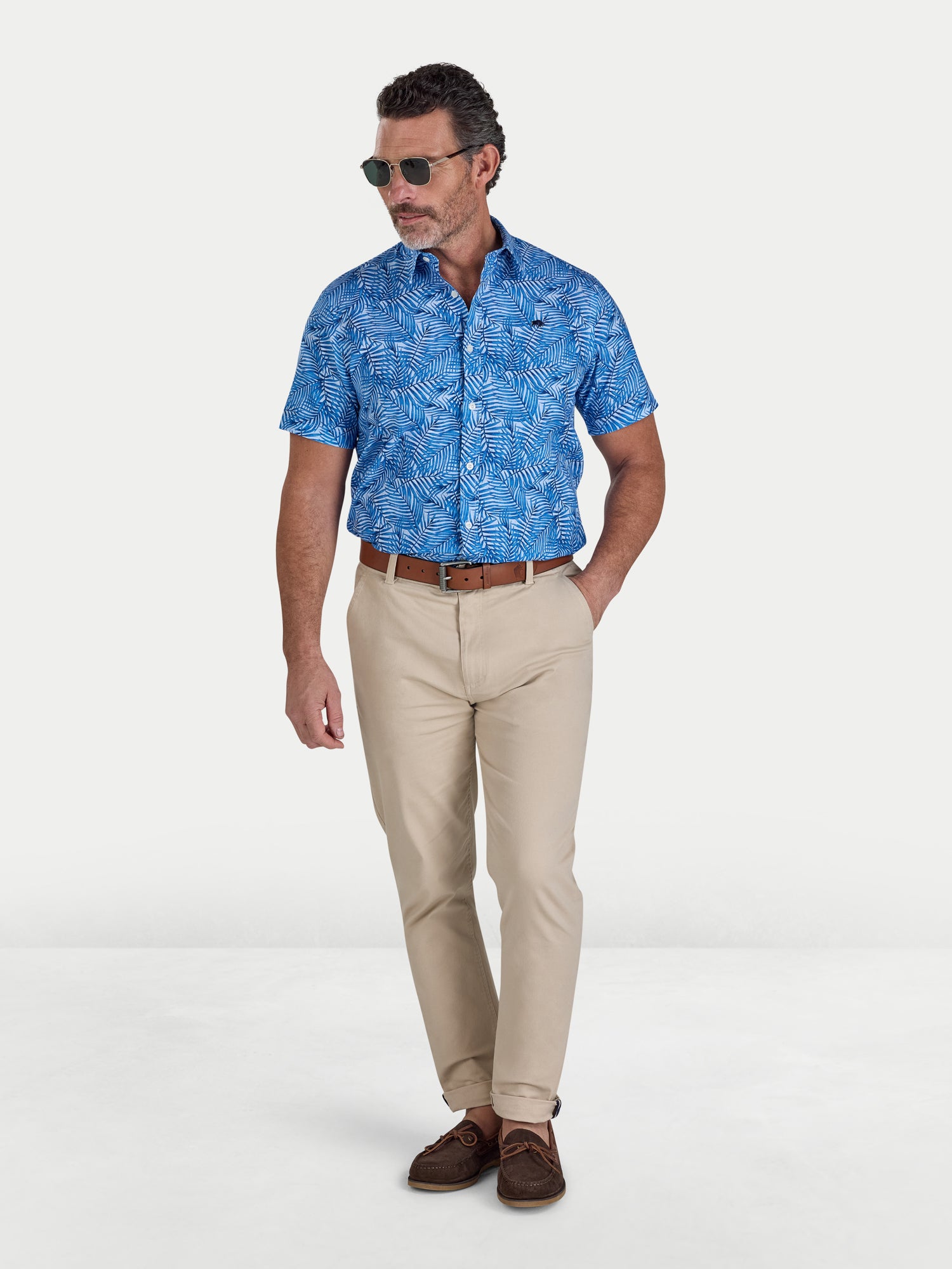 Man wearing a blue patterned shirt, beige pants, and brown shoes on a white background