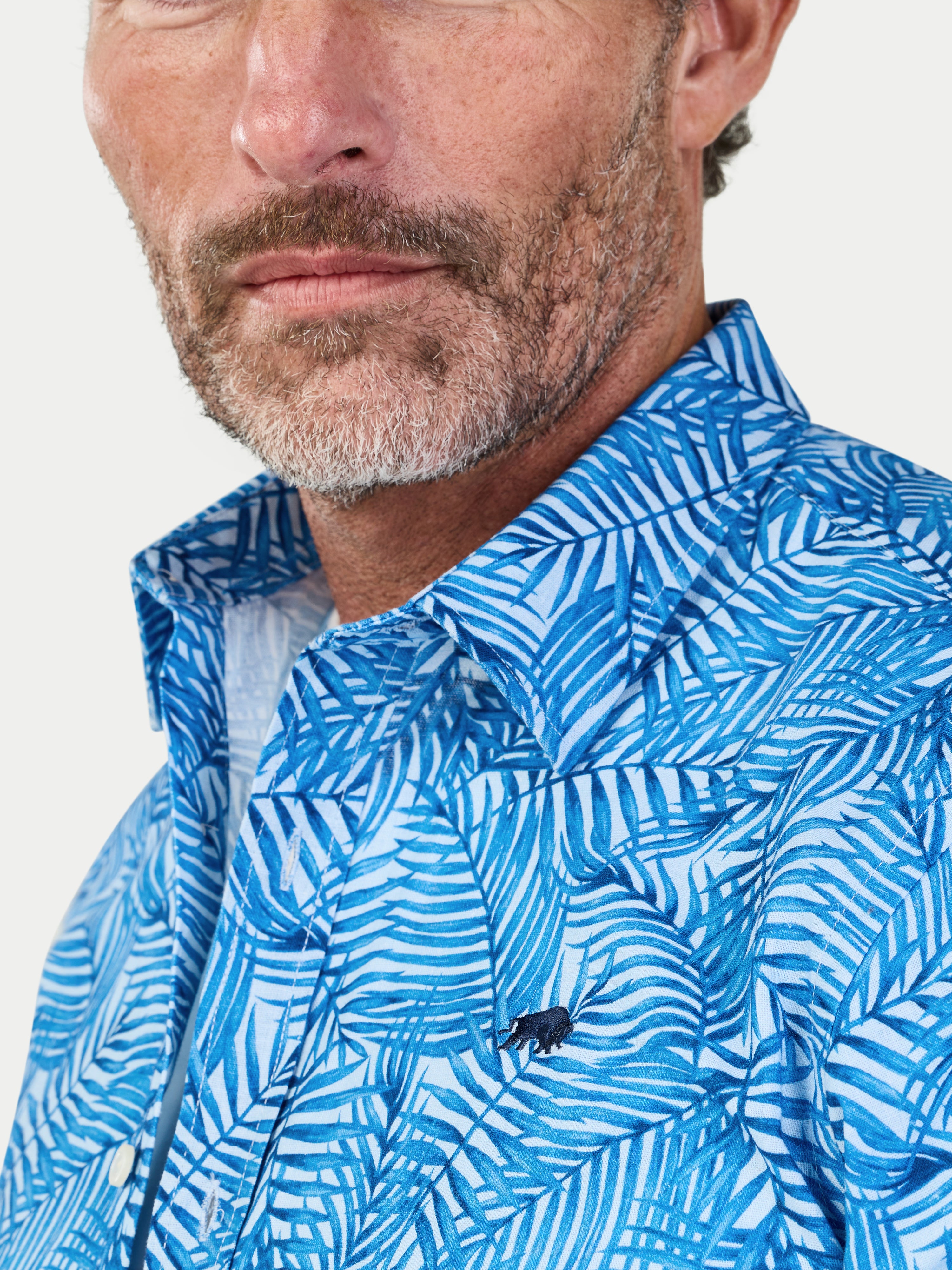 Man wearing a blue patterned shirt with a brand logo on a white background