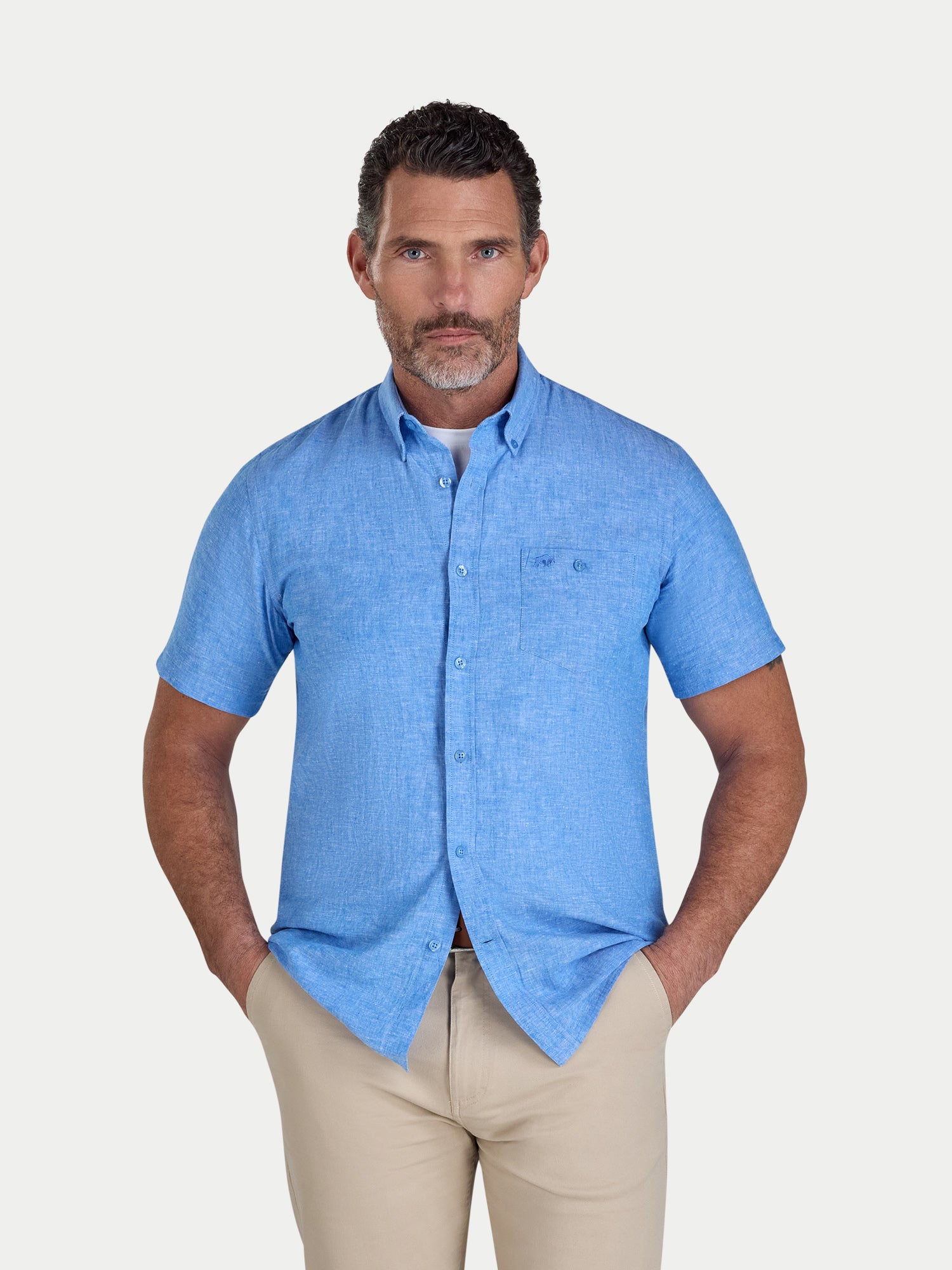 Man wearing a blue short-sleeve shirt and beige pants on a light gray background