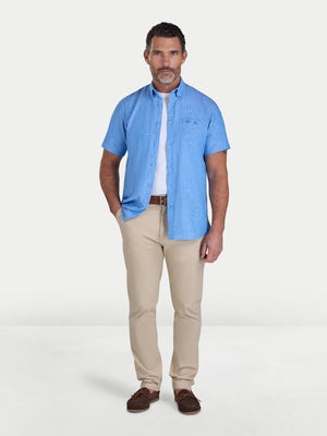 Man wearing a blue shirt, white undershirt, beige pants, and brown shoes on a white background