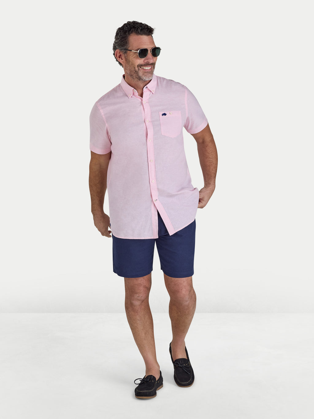 Man wearing a pink shirt and navy shorts on a white background