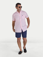 Man wearing a pink shirt and navy shorts on a white background